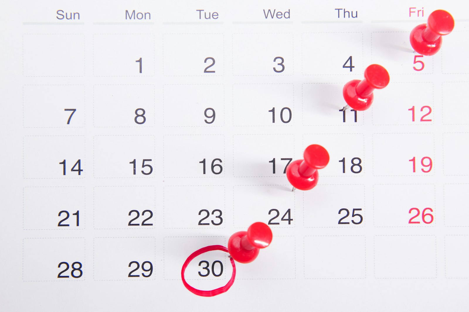 A wall calendar with red pins marking dates, with the 30th circled in red